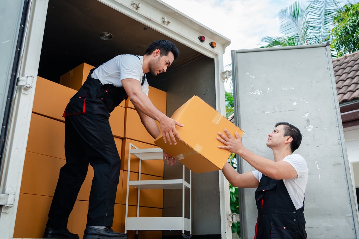Movers unloading boxes and furniture from a truck outside a new house