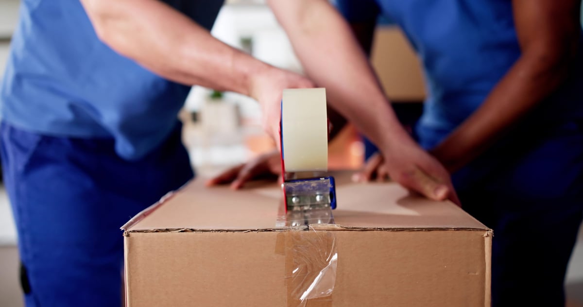 Movers packing cardboard boxes with tape to prepare for a move