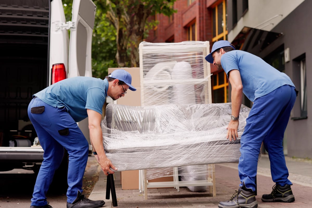 Two professional movers unloading furniture from a truck outside a client's home